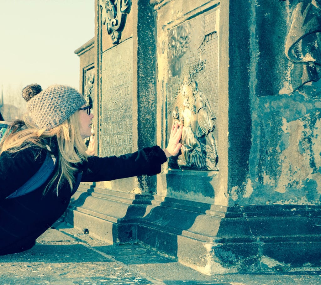 Making a wish on the Charles Bridge in Prague. Avoid the crowds in Prague and on the Charles Bridge by visiting in the morning.